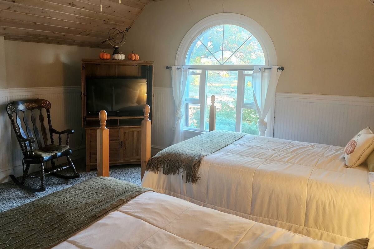 A room with a bed, a rocking chair, a television, and a window with a view of the outdoors.