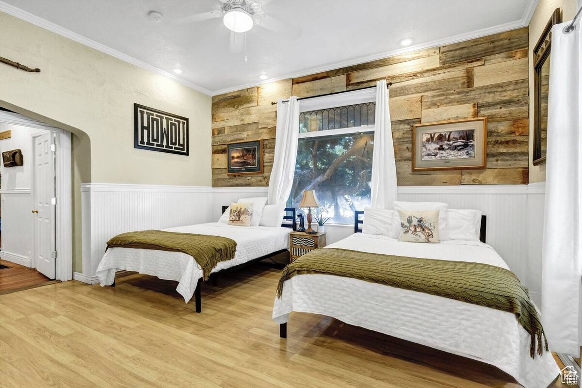 A bedroom with two beds, a wooden accent wall, a window with a view, and a door.