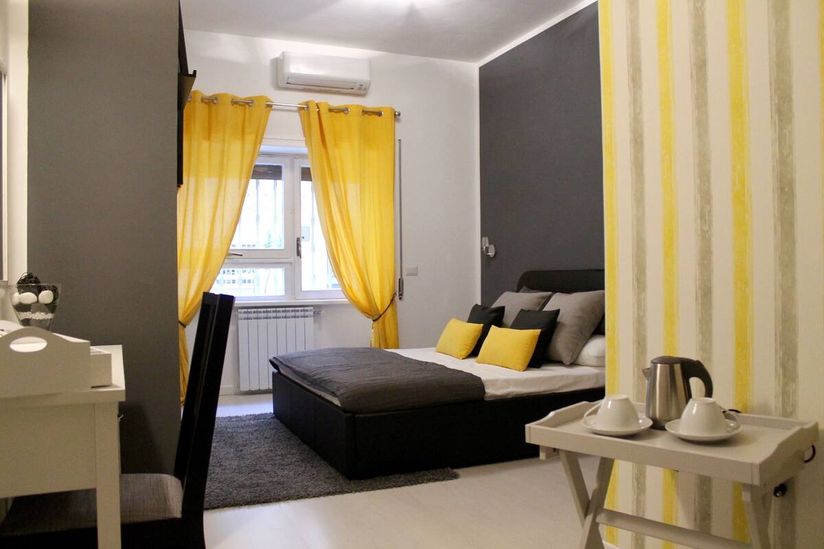 A bedroom with a bed, a bedside table, a chair, curtains, and a radiator.