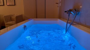 A bathtub with blue lighting, a control panel, and a showerhead. - Le Coq Suites (Rome)