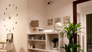 A room with a wall clock, a globe, a welcome sign, shelves with decorative items, and a potted plant. - Le Coq Suites (Rome)