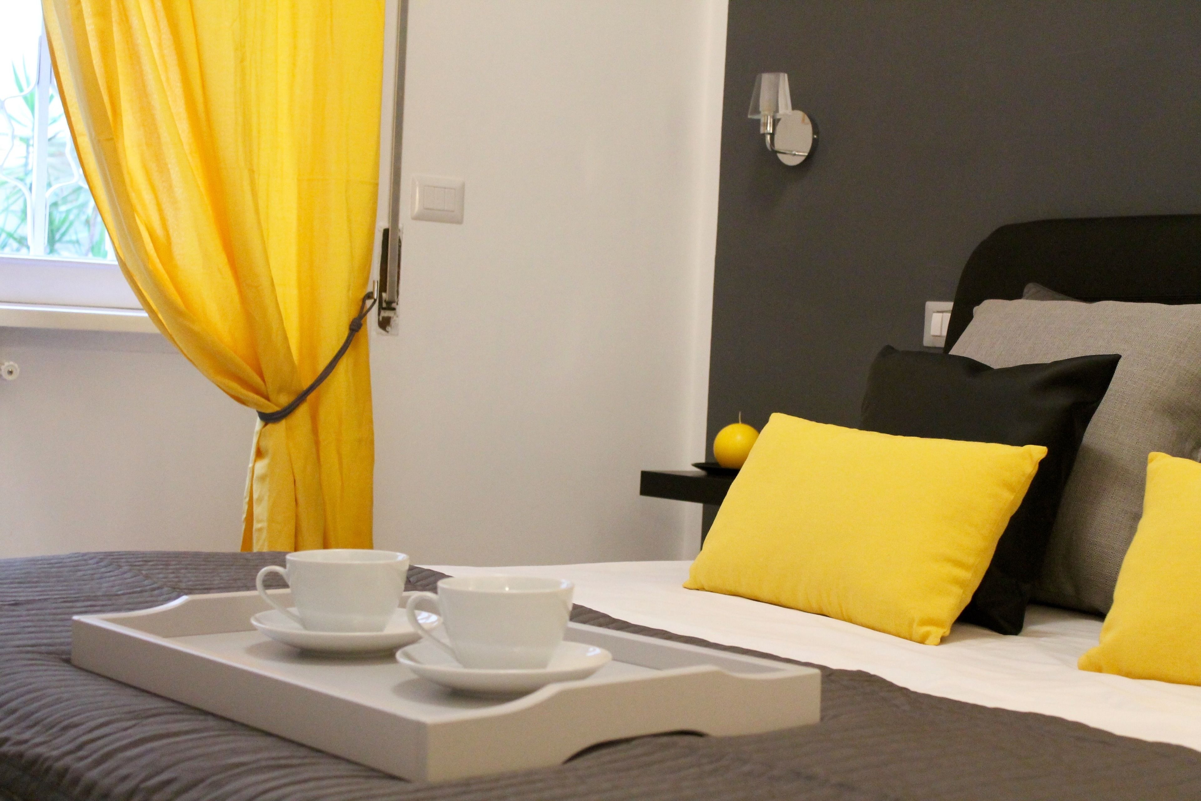 Una habitación de hotel con una cama, una bandeja con dos tazas y una ventana con cortinas amarillas.