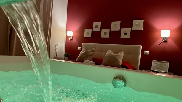 A bathroom with a bathtub, a mirror, and a red wall with light switches. - Le Coq Suites (Rome)
