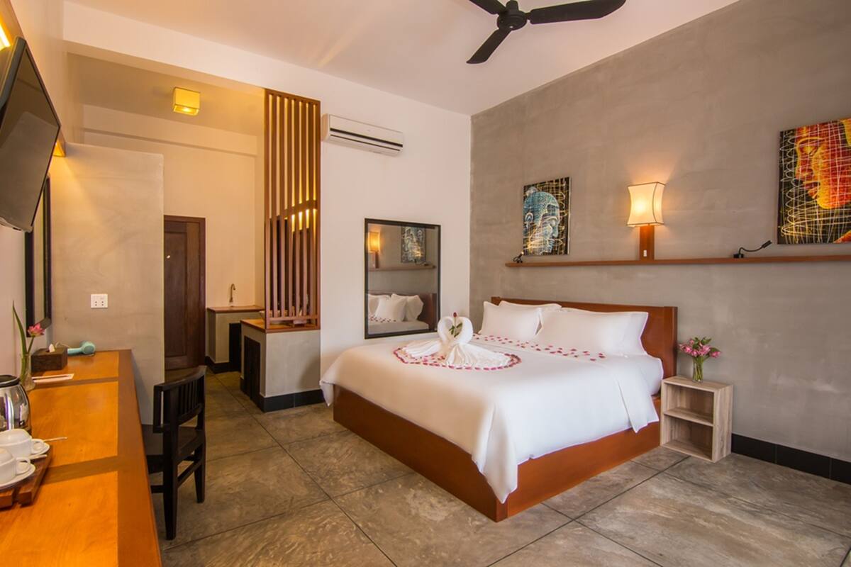 A hotel room with a large bed, a desk, a chair, a TV, and artwork on the walls.