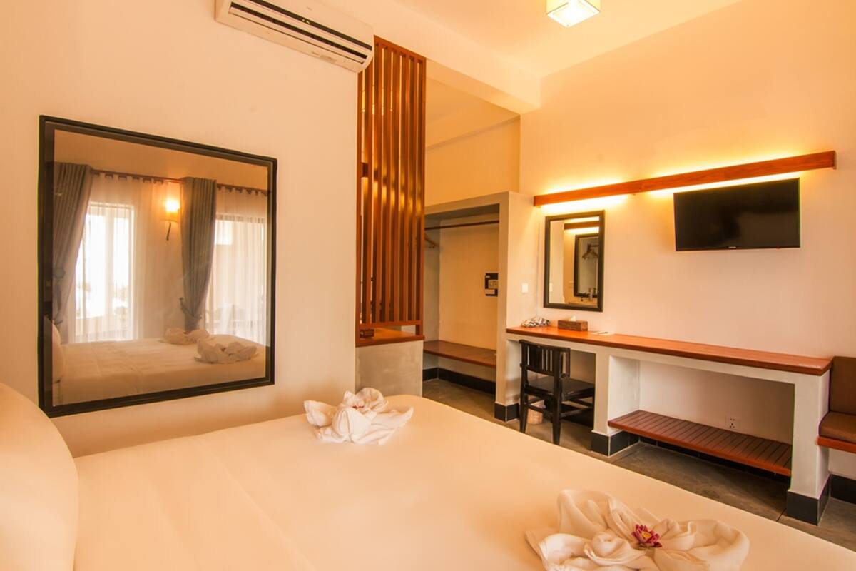 A hotel room with a large bed, a desk, a chair, a TV mounted on the wall, and a mirror.