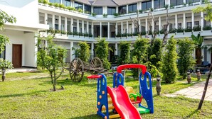 A courtyard with a playground, a building with balconies, and a traditional wooden cart. - Ompil Angkor Residence (Siem Reap)