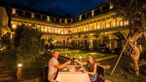 A couple dining at an outdoor table with a view of a pool and a building with multiple balconies. - Ompil Angkor Residence (Siem Reap)