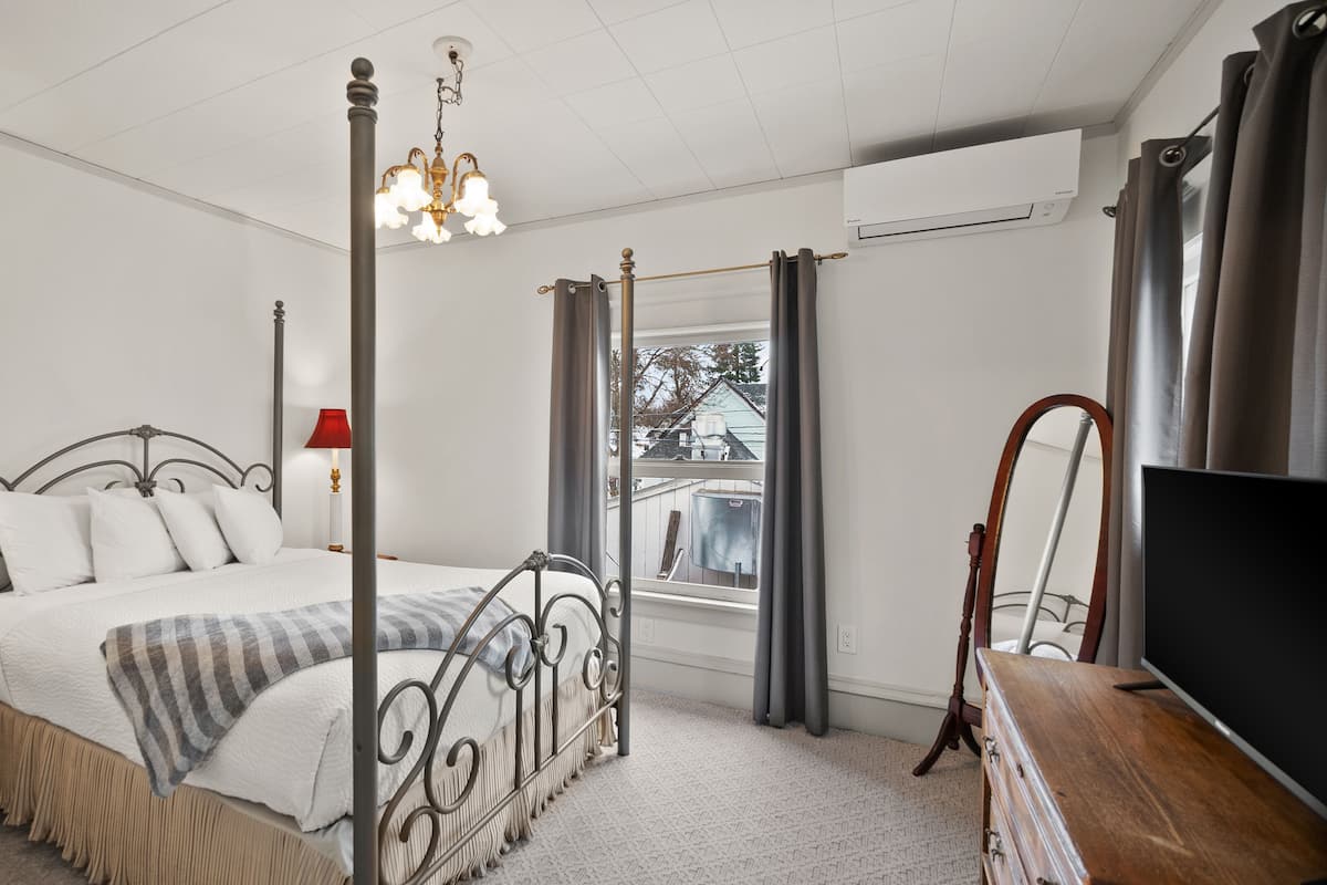 A bedroom with a four-poster bed, a television, and a window with curtains.
