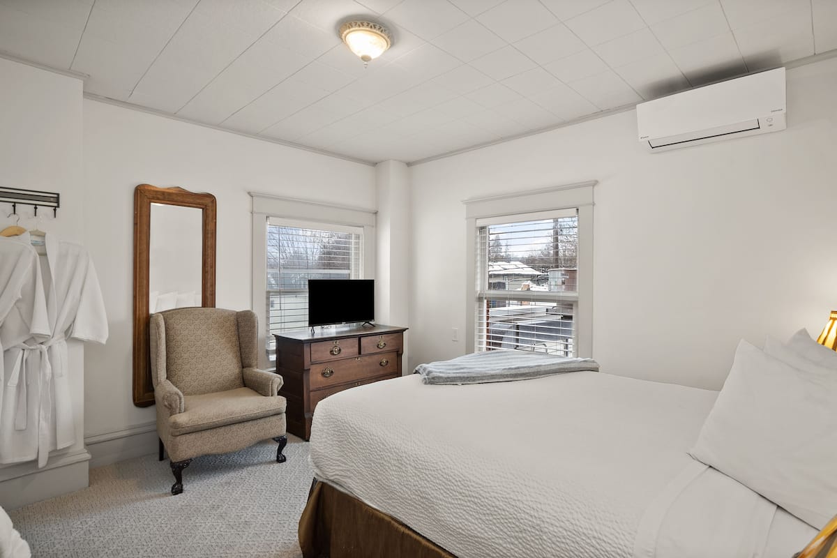 A bedroom with a bed, a dresser, a chair, a TV, and a window with blinds.