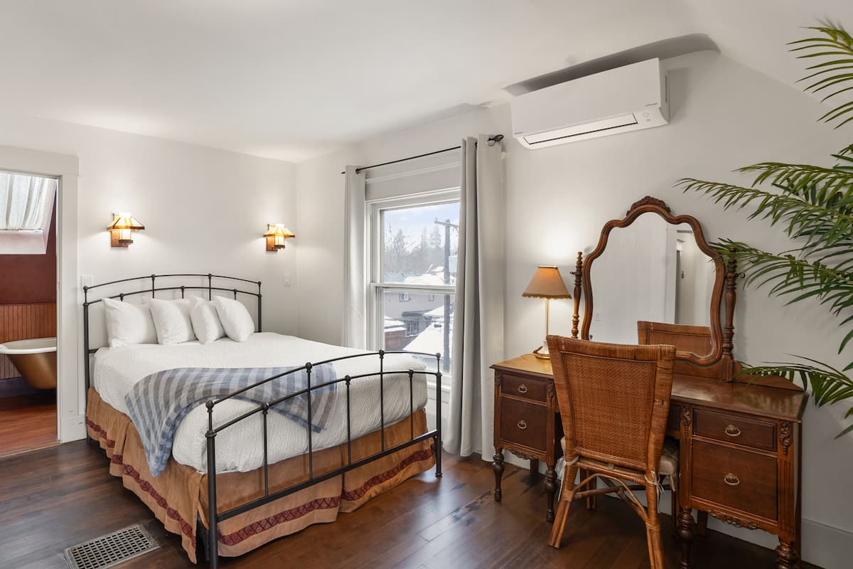 A bedroom with a bed, bedside table, chair, dresser, and an air conditioning unit.