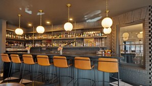 Un espace bar doté de nombreux tabourets, d’un comptoir bien garni de bouteilles variées et de luminaires sphériques suspendus.