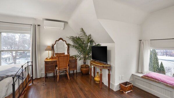 A bedroom with a bed, dresser, mirror, television, potted plant, and a window with a view of trees.