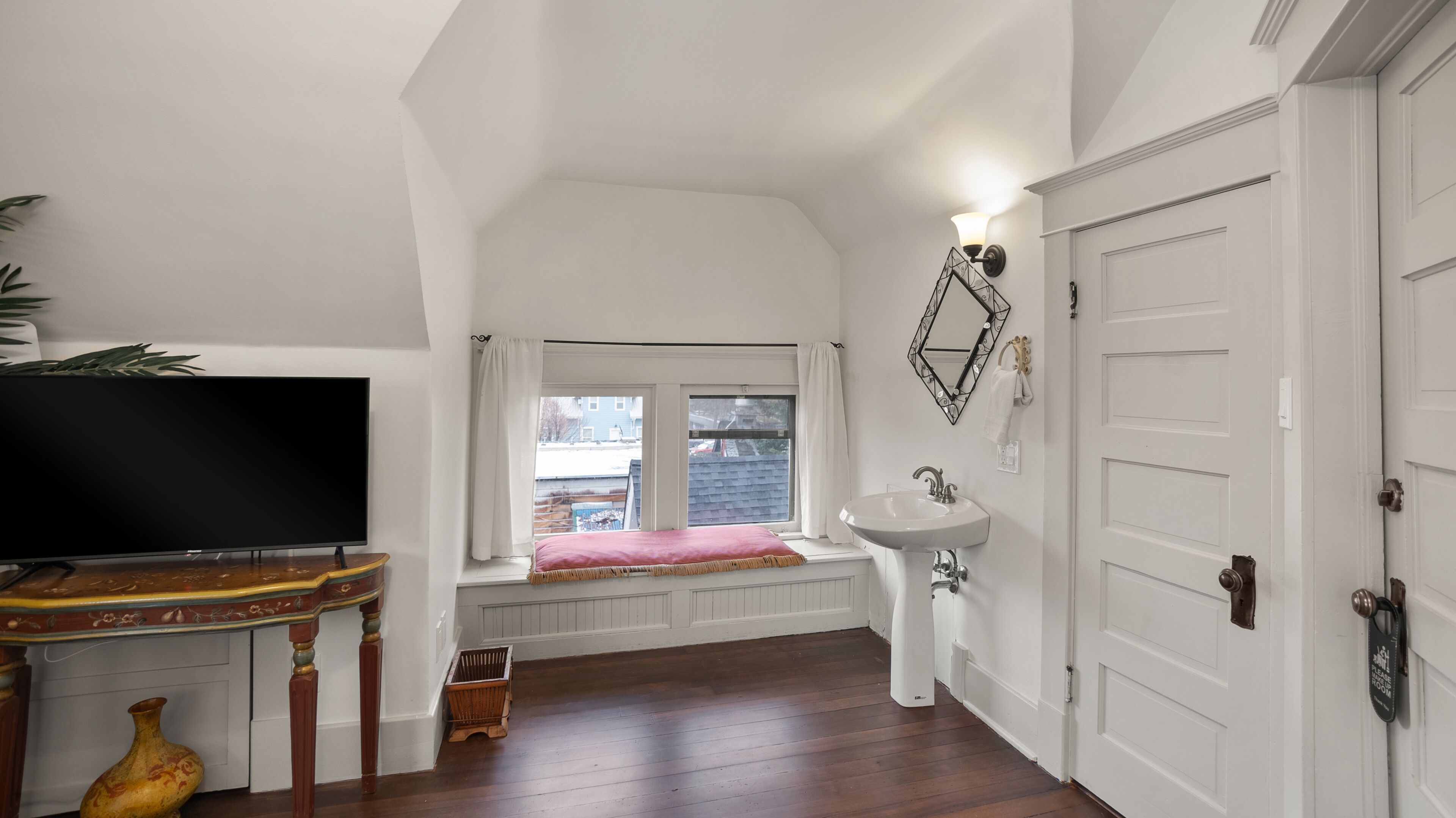 Ein Zimmer mit Holzboden, Fernseher, Spüle, Spiegel und einer Tür.