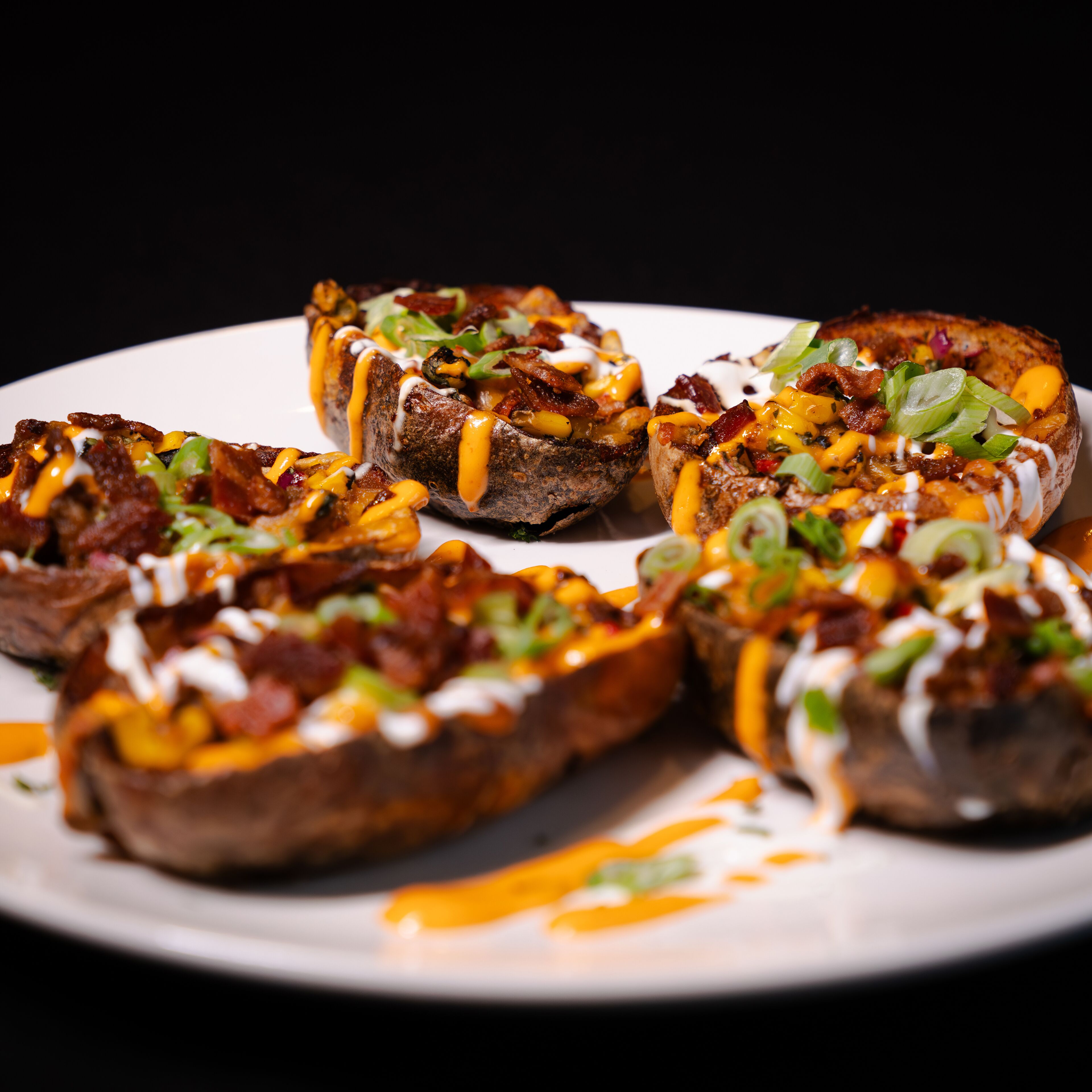Un plato de papas al horno cubiertas de queso, tocino y cebollines.