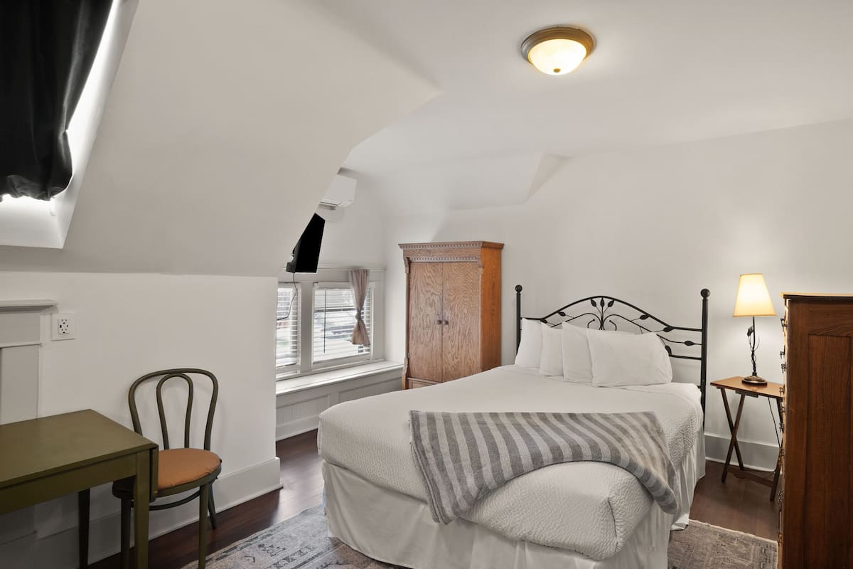 A bedroom with a bed, a wooden wardrobe, a desk, and a chair.