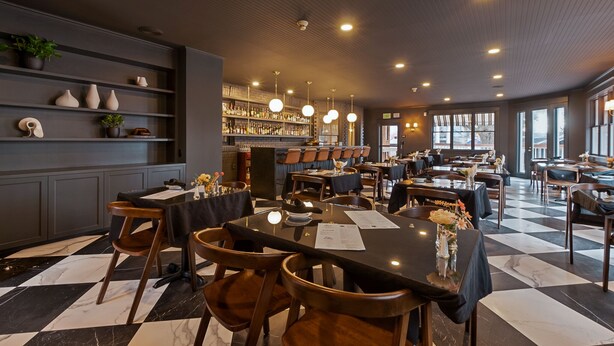 Un restaurant avec un sol à carreaux, des chaises en bois et des tables où sont disposés des menus.