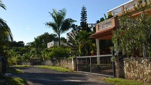A gated entrance to a property with a stone wall and metal gate, surrounded by lush greenery and a clear blue sky. - Apartments with Balcony in the Villa, Pool (Sosúa)