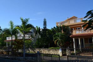 Un grand bâtiment doté d’un balcon, entouré de palmiers et d’un mur de pierre.