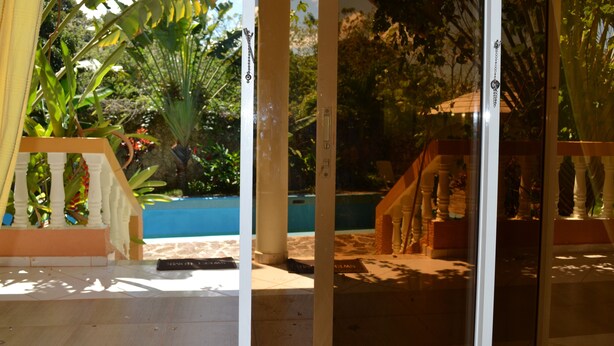 A glass door leading to a covered outdoor area with a pool, palm trees, and a wooden staircase. - Apartments with Balcony in the Villa, Pool (Sosúa)