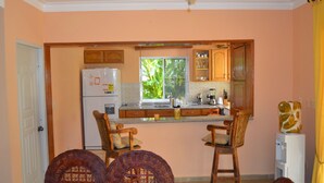 A kitchen with wooden cabinets, a refrigerator, a sink, and two wicker chairs. - Apartments with Balcony in the Villa, Pool (Sosúa)