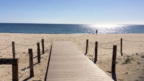 A wooden boardwalk leading to a beach with a clear sky and calm sea. - Camping Flumendosa (Pula)