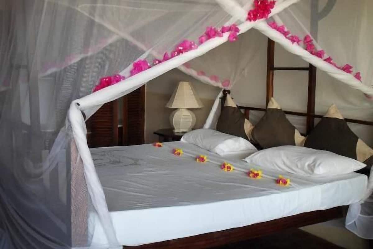 Una cama con dosel, almohadas y una mesita de noche con lámpara.