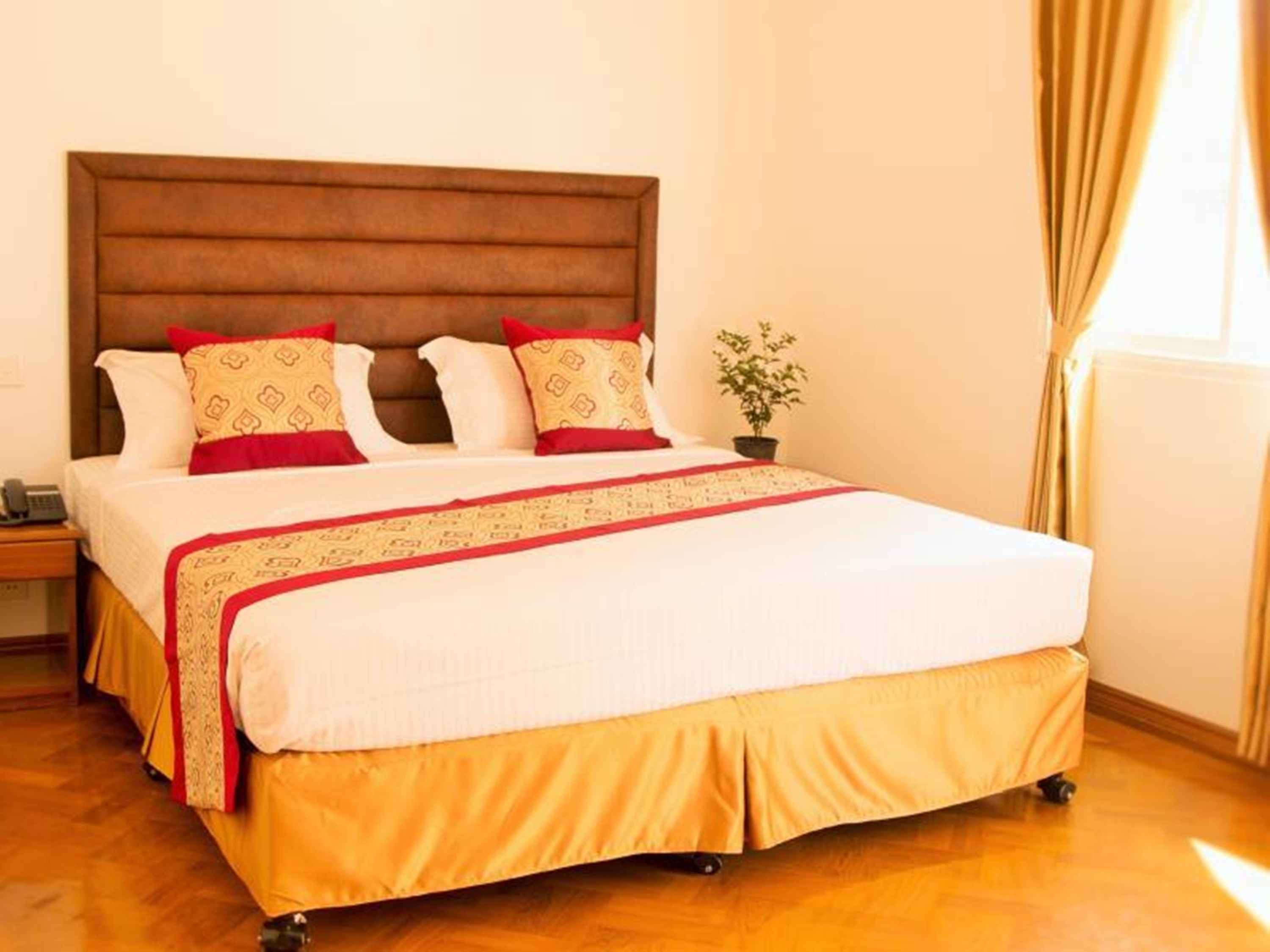 A hotel room with a large bed, a wooden headboard, and a small potted plant.