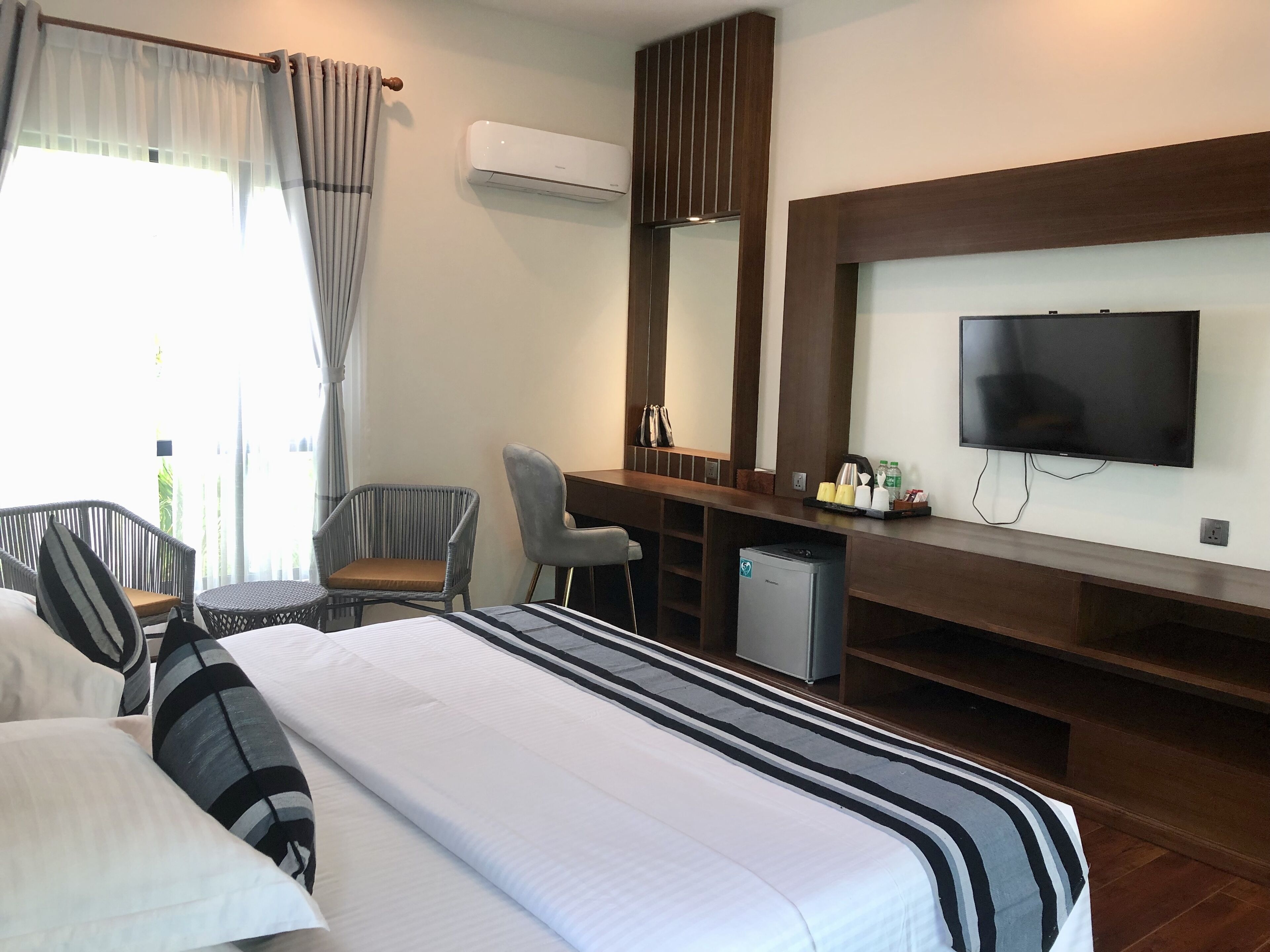 A hotel room with a bed, a desk, a chair, a television, and an air conditioning unit.