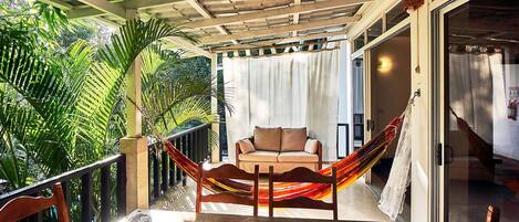 A covered balcony with a table and chairs, a hammock, and a sofa with cushions.