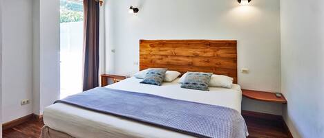 A bedroom with a wooden headboard, a bed with a grey blanket, two pillows, a bedside table, and a nightstand.