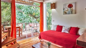 Una habitación con piso de madera, un sofá rojo, una mesa de centro de madera y un balcón con mesa y sillas.
