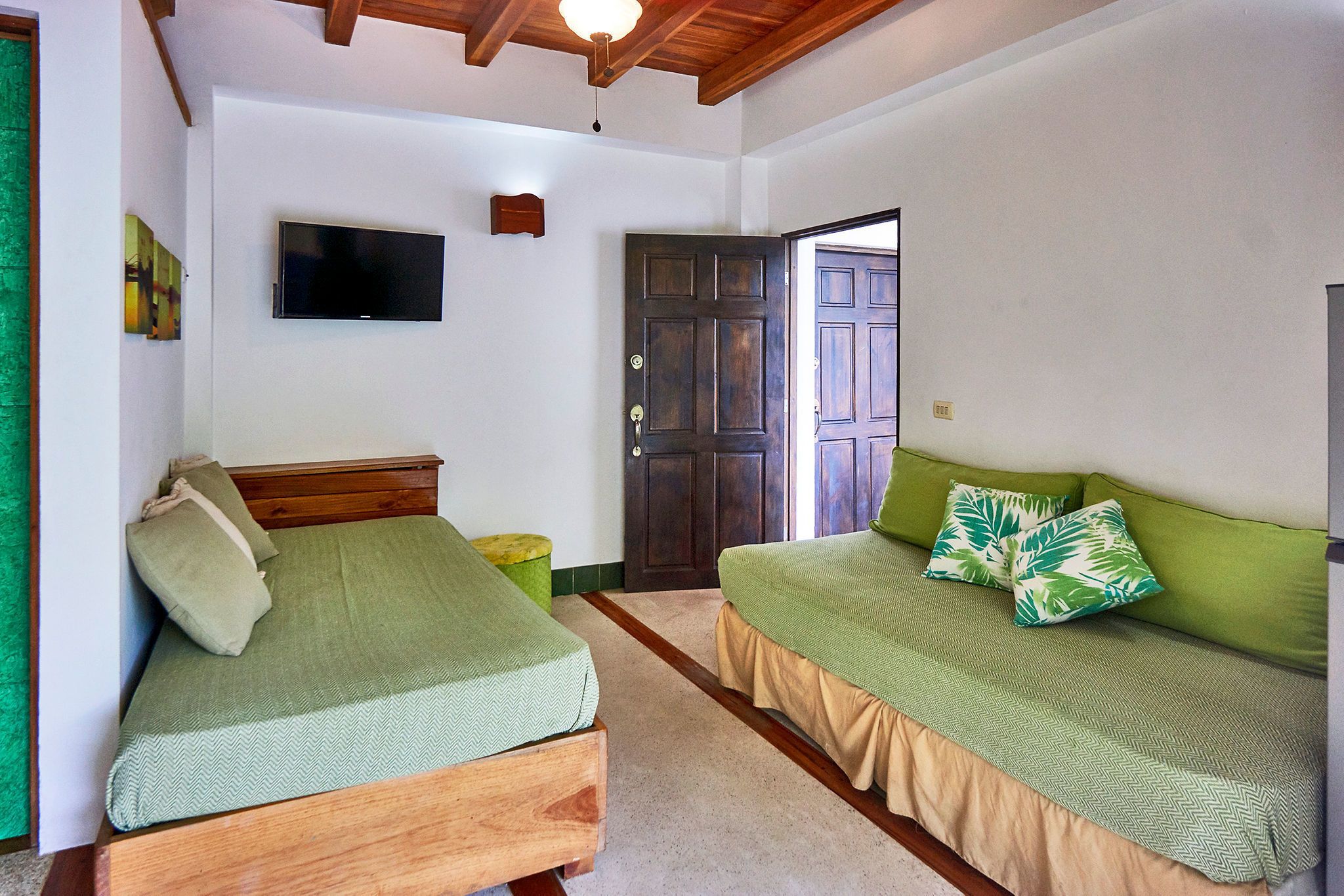 Un dormitorio con dos camas de madera, un televisor en la pared y una puerta que da al exterior.