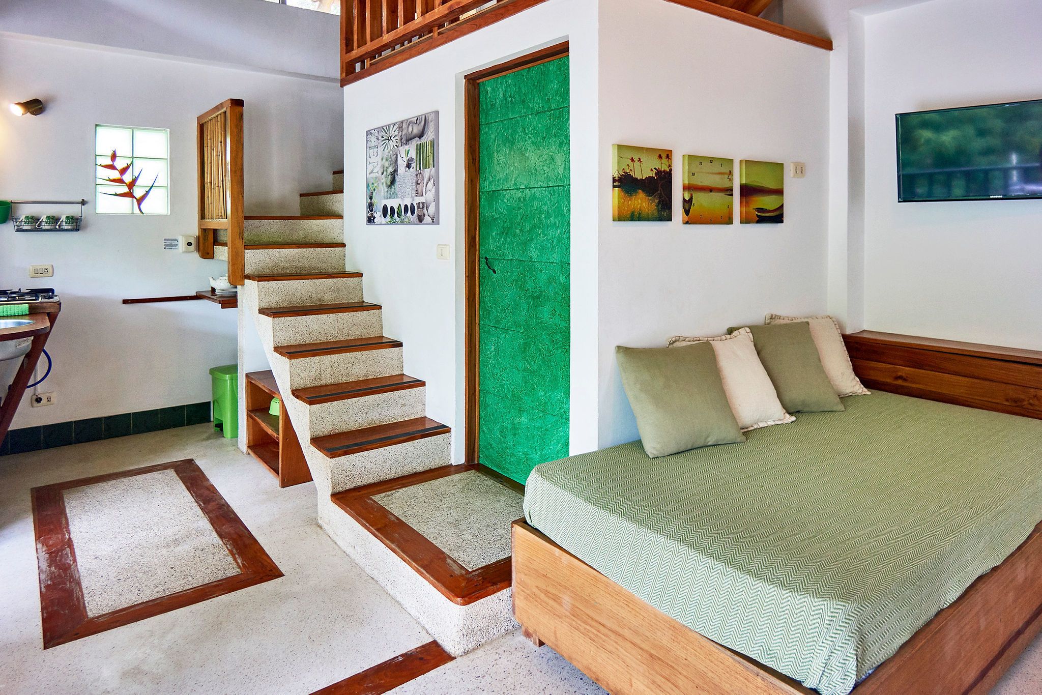 A bedroom with a bed, a green door, a staircase, and artwork on the walls.