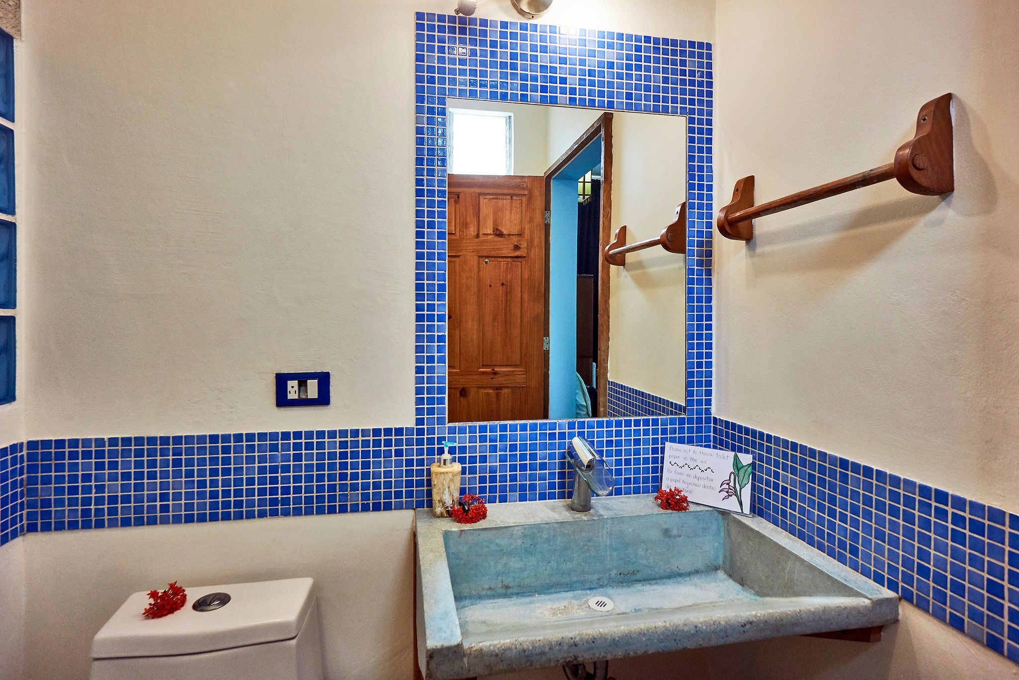 Un baño con pared de azulejos azules, un inodoro blanco, un lavabo con espejo y una puerta de madera.
