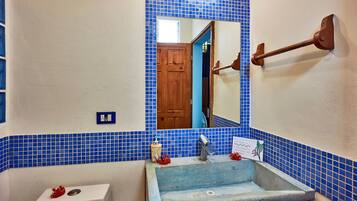 Un baño con pared de azulejos azules, un inodoro blanco, un lavabo con espejo y una puerta de madera.