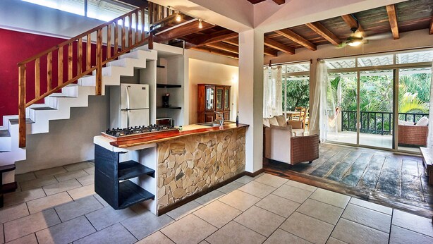 Una cocina amplia con una isla de piedra, una escalera de madera y un amplio ventanal corredera que da a un balcón.