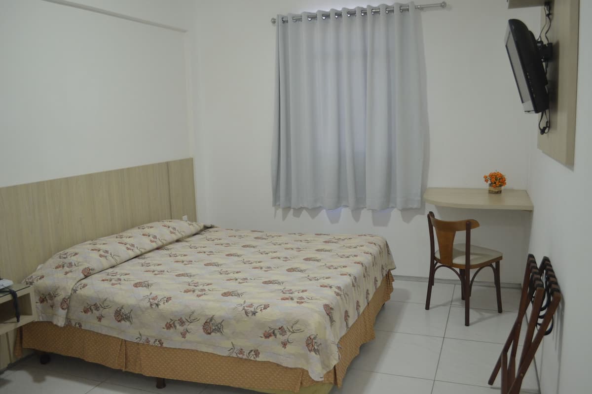 A bedroom with a bed, a desk, a chair, and a TV mounted on the wall.