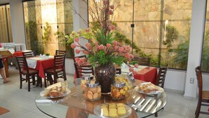 Un comedor con una mesa de vidrio rodeada de sillas, un florero con flores y diversos alimentos en recipientes.