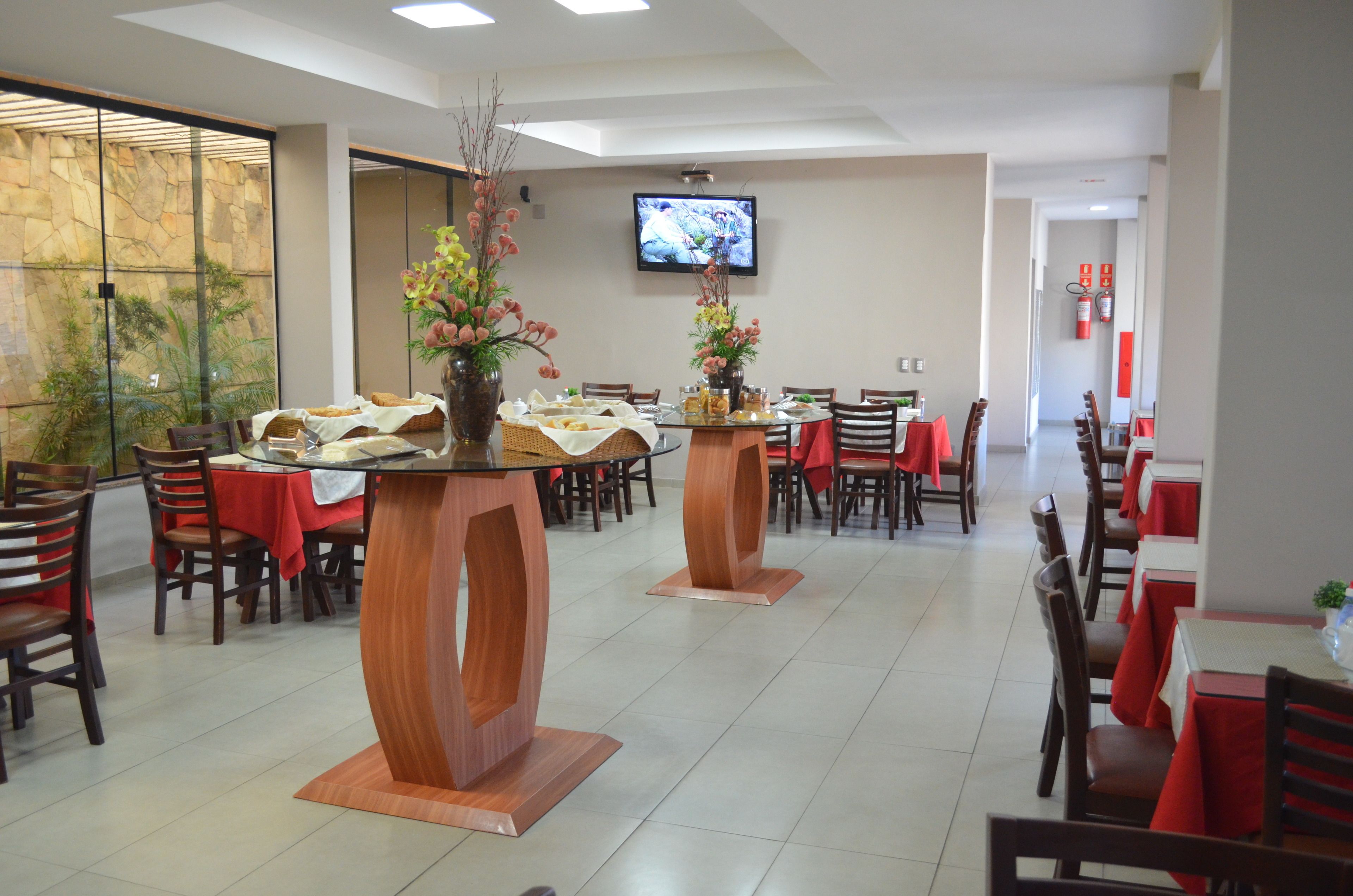 Um restaurante com várias mesas e cadeiras, uma televisão presa à parede e uma parede de pedra com plantas.