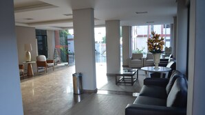 Un vestíbulo amplio con diseño moderno, que incluye un área de descanso con sofás y sillones, una mesita y un jarrón decorativo.