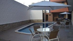 Un área de piscina en la azotea con una piscina pequeña, sillones de descanso y sombrillas.
