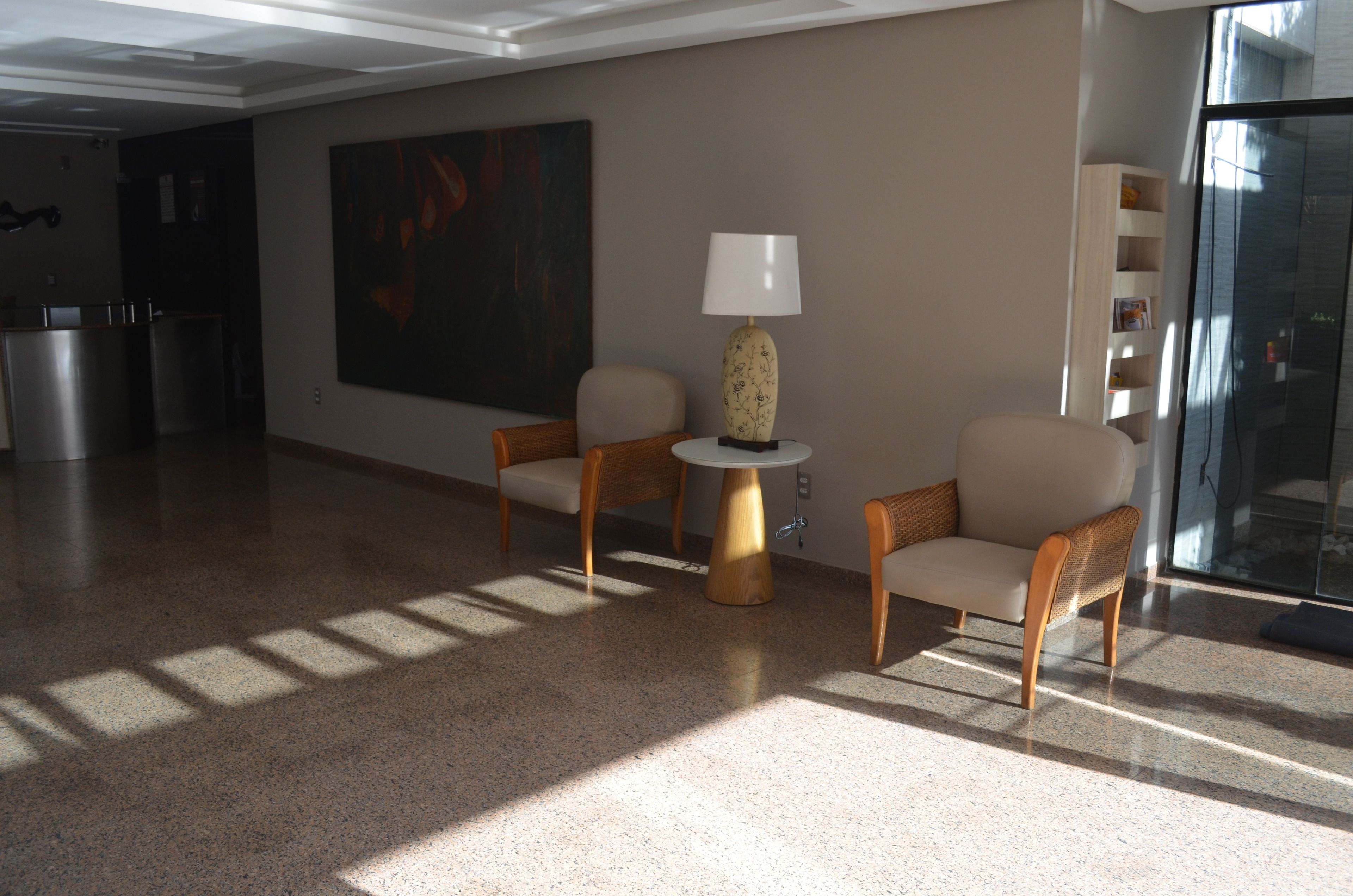 A spacious lobby with two chairs, a table with a lamp, a large abstract painting, and a glass partition.