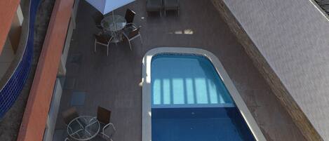 Uma área de piscina com uma piscina retangular, rodeada por espreguiçadeiras e guarda-sóis.