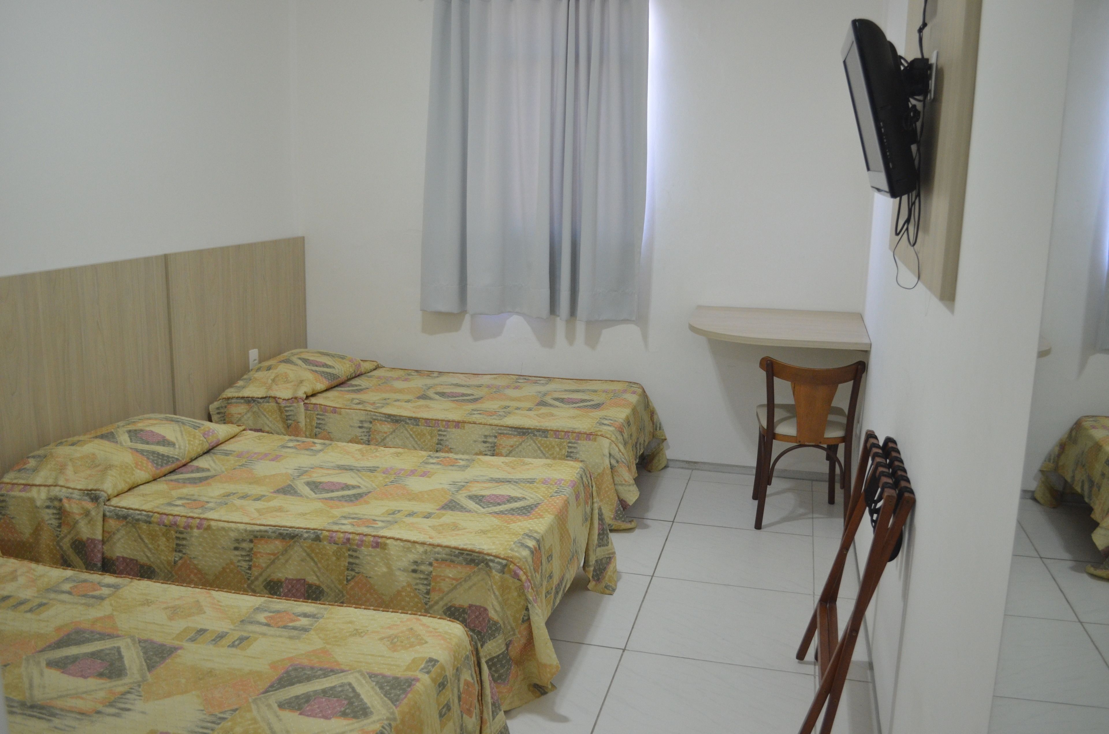 A room with four beds, a desk, a chair, and a television mounted on the wall.