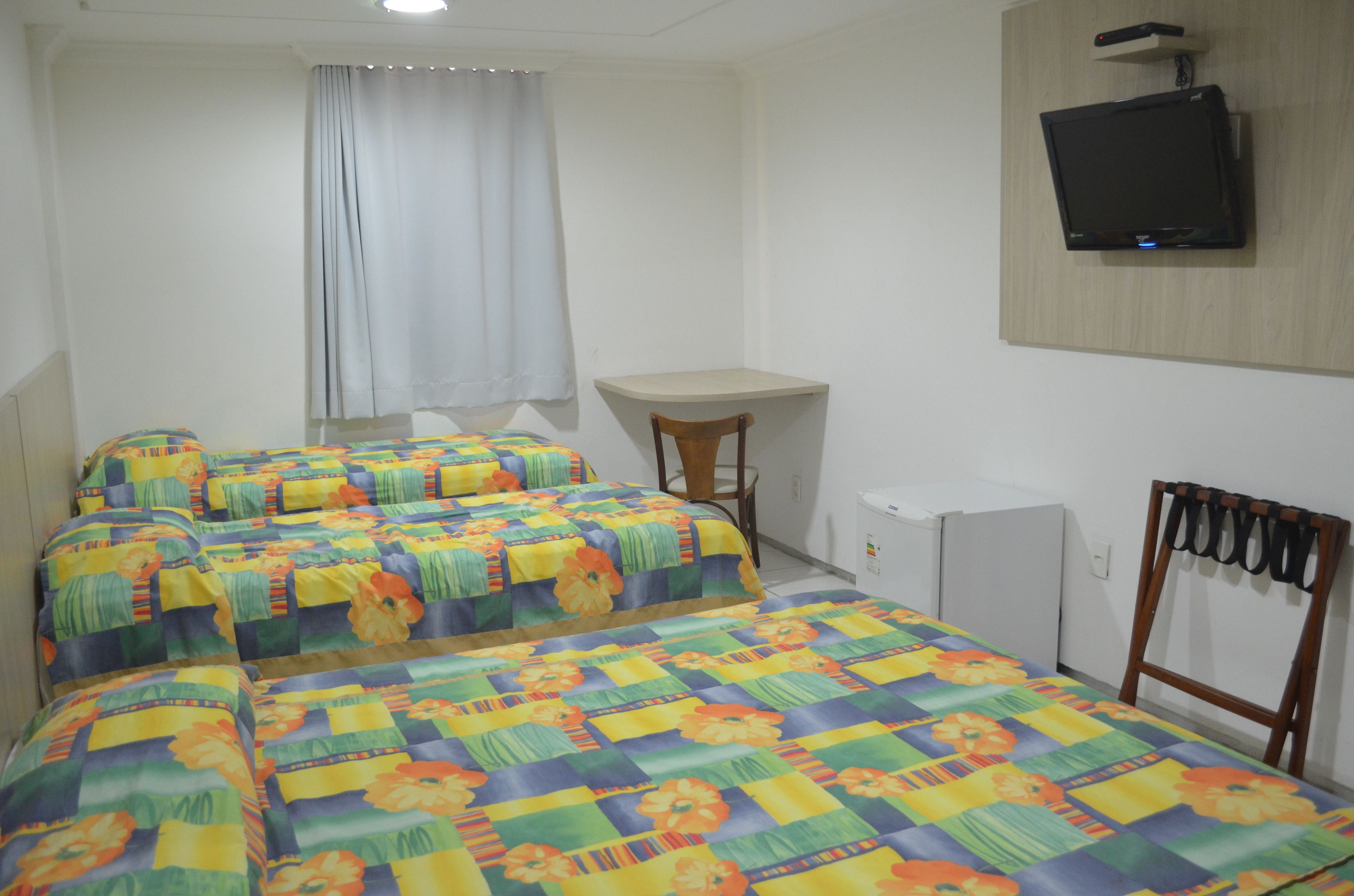 A room with two beds, a desk, a chair, and a television mounted on the wall.