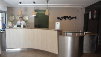 A reception desk with a man standing behind it, three wall clocks, and a modern light fixture.