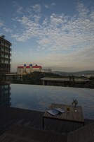 An infinity pool with a wooden deck and a table with a glass of drink and a book.