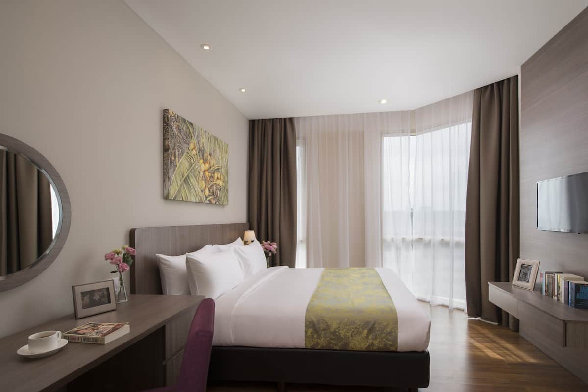 Ein modernes Hotelzimmer mit einem großen Bett, einem Schreibtisch mit Stuhl, einem Fernseher und einem Fenster mit Vorhängen.