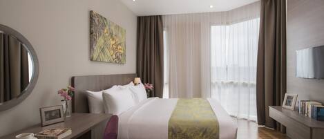 A modern hotel room with a large bed, a desk with a chair, a TV, and a window with curtains.
