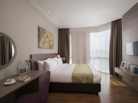 A modern hotel room with a large bed, a desk with a chair, a TV, and a window with curtains.
